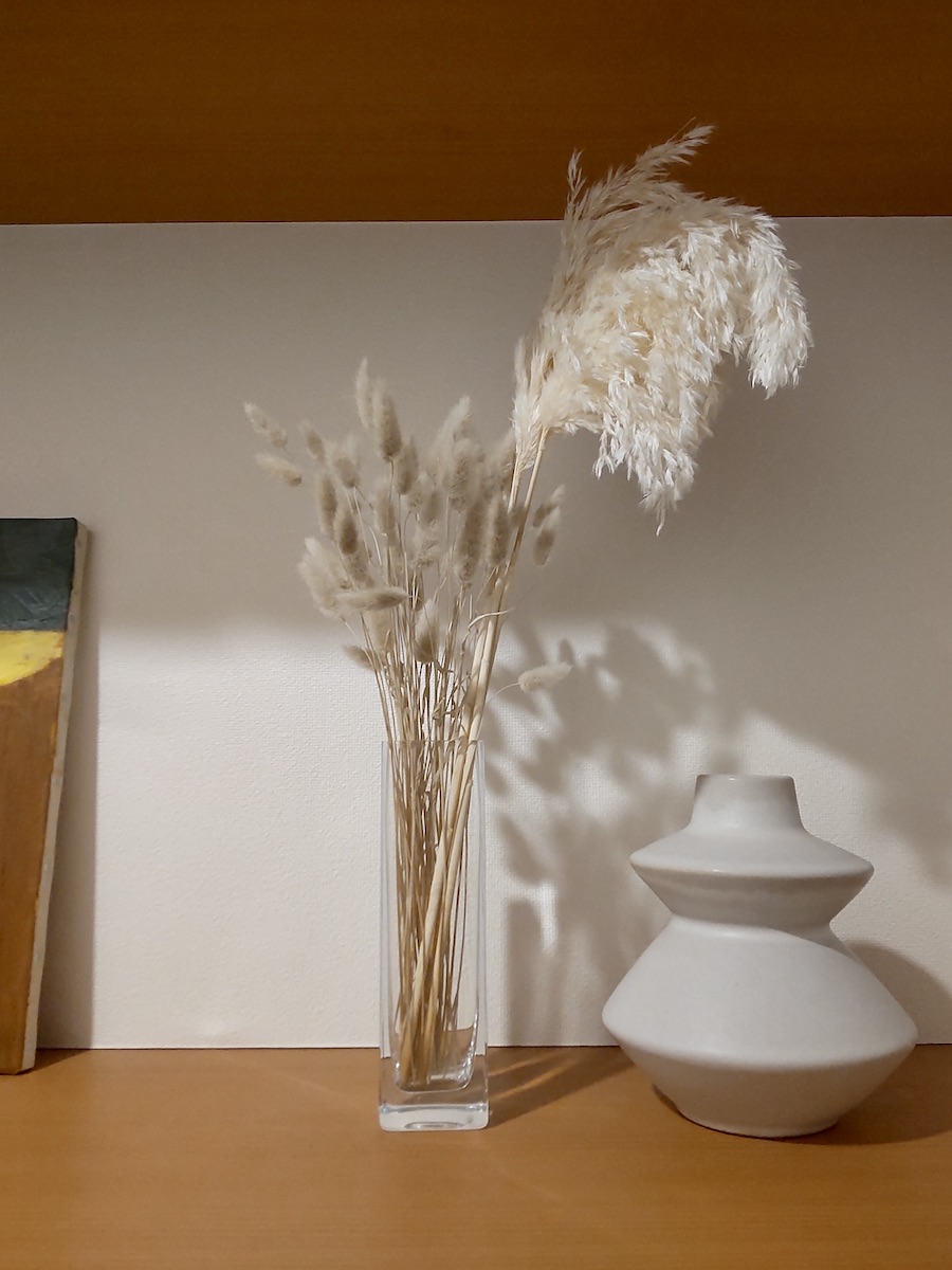 Dried gray bunny tail grass and white dried wheat in glass vase, displayed beside an empty white vase at the entrance