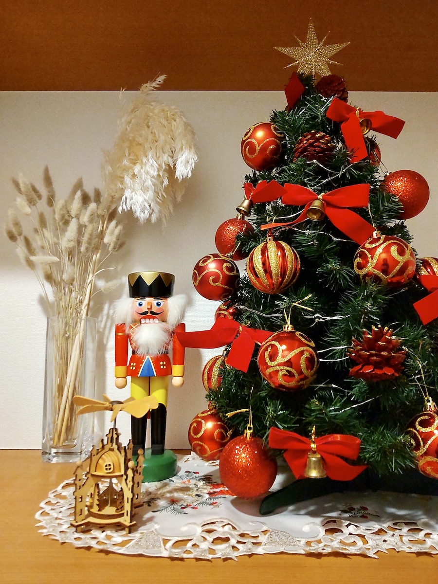 A Christmas tree richly decorated with red ornaments, accompanied by a nutcracker, white dried flowers, and wooden toys