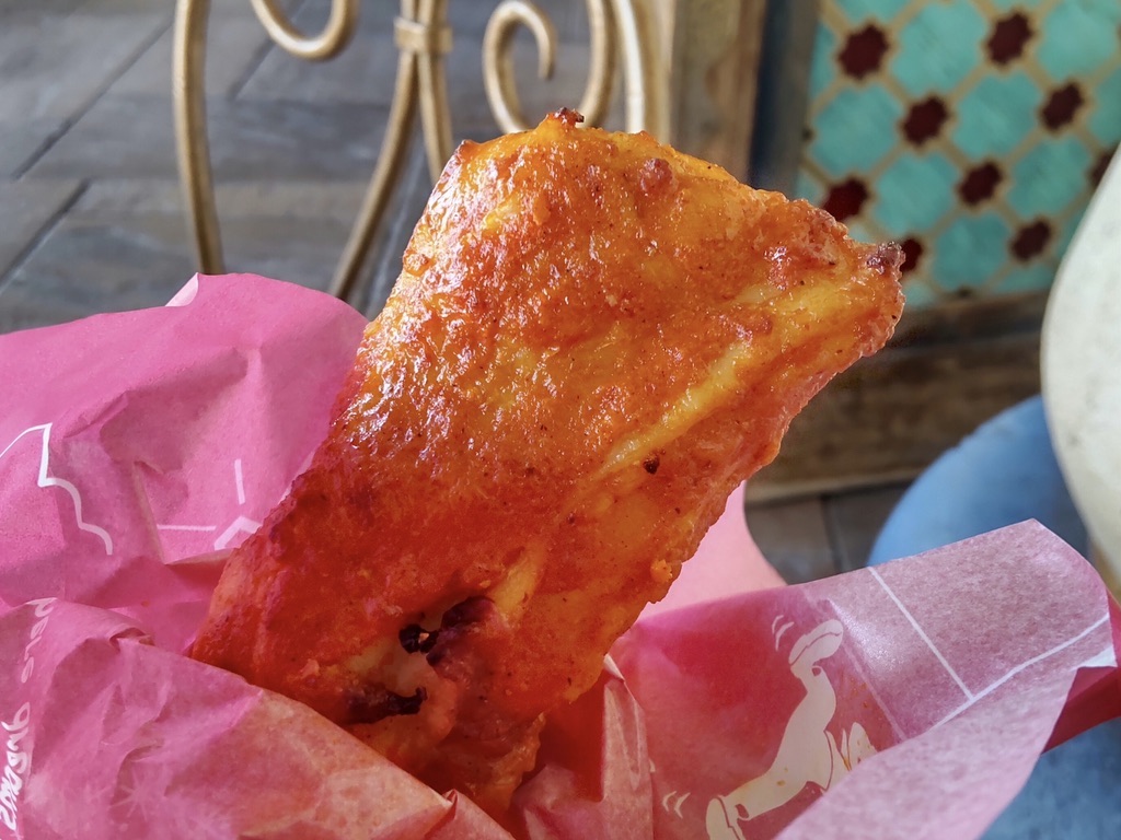 A close-up of tandoori chicken held up against the background of the Casbah Food Court terrace