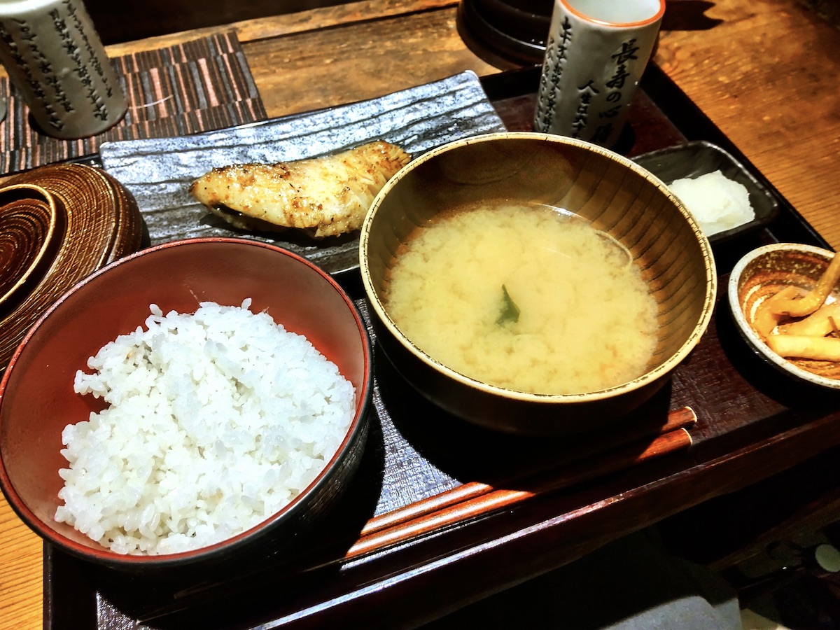 A Japanese set meal featuring a thick slice of charcoal-grilled fish, served with a bowl of rice and miso soup